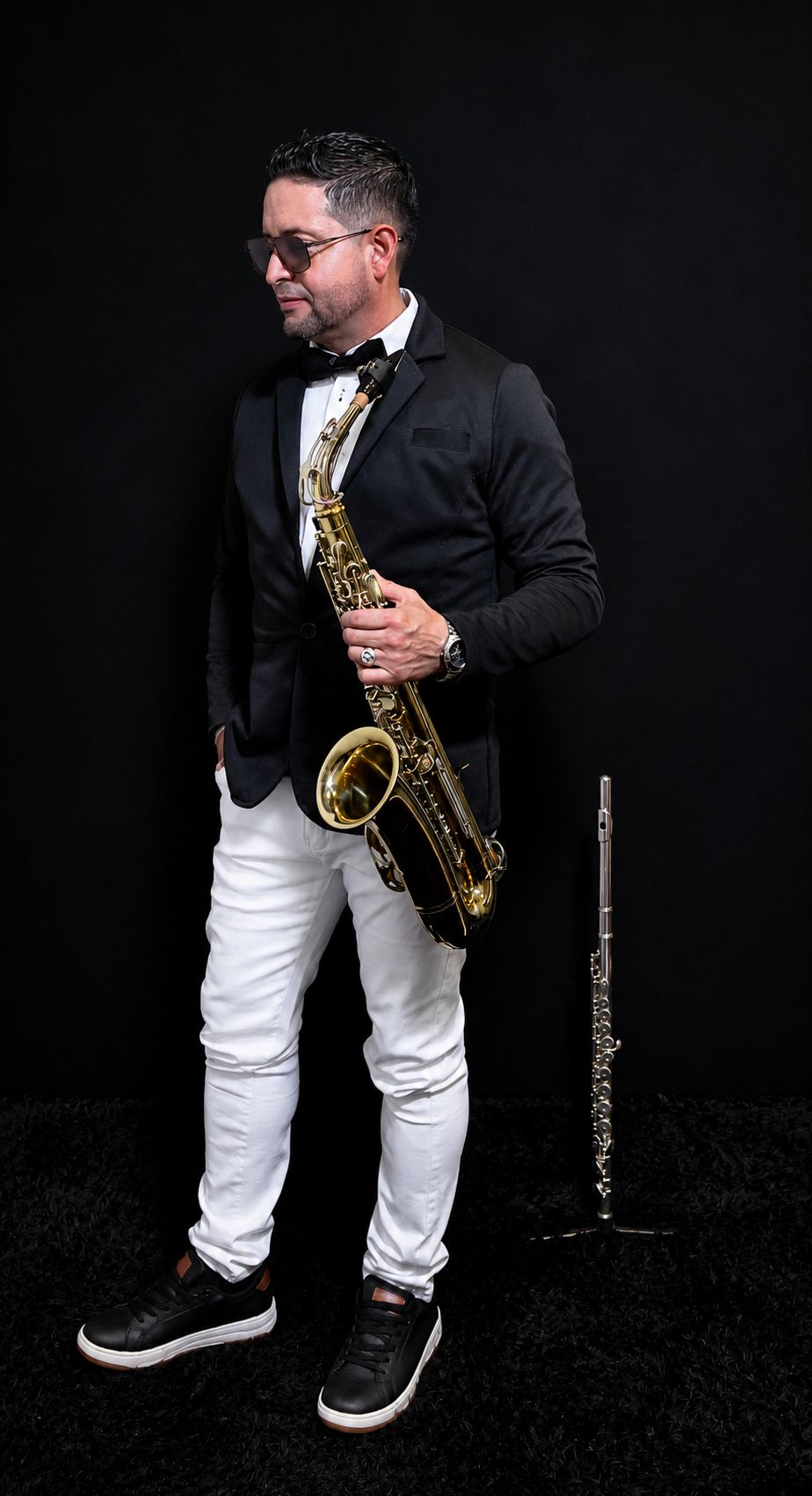 Saxofonista en Bogotá con smoking negro sosteniendo un saxofón tenor dorado junto a una flauta traversa