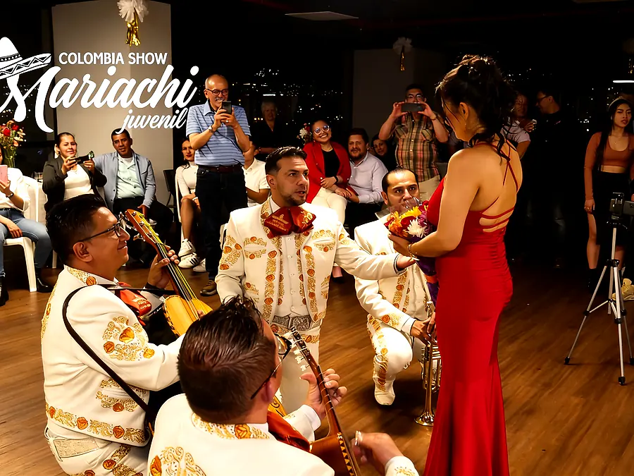 Mariachi de rodillas entregando flores a una mujer de vestido rojo durante una serenata sorpresa en Bogotá
